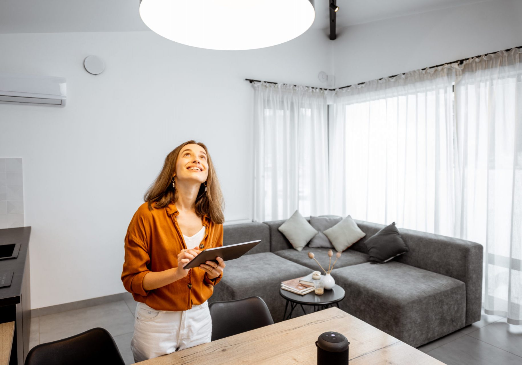 Young woman controlling home light with a digital tablet in the living room. Concept of a smart home and light control with mobile devices